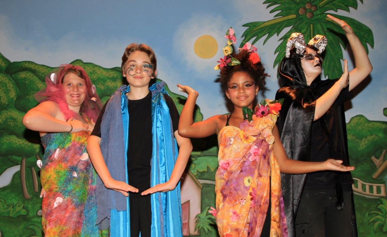 Actors in bright costumes in front of a tropical backdrop