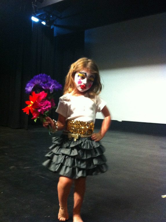 A young performer in clown makeup holding flowers