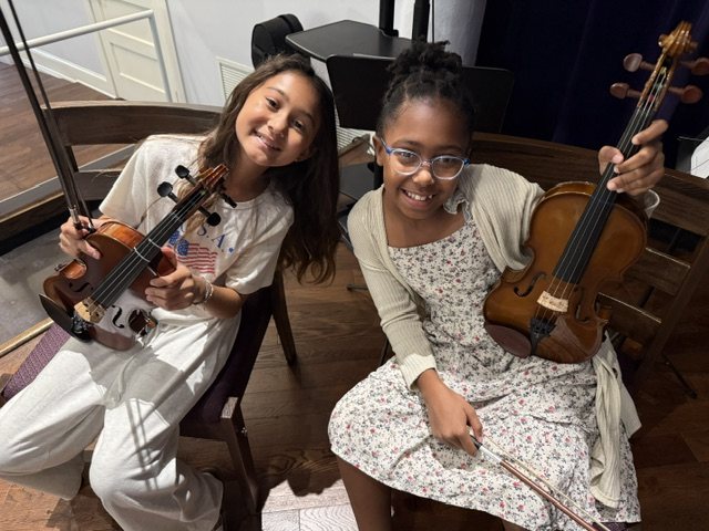 Two young violinists smile with their violins